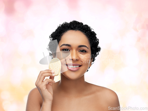 Image of young woman cleaning face with exfoliating sponge