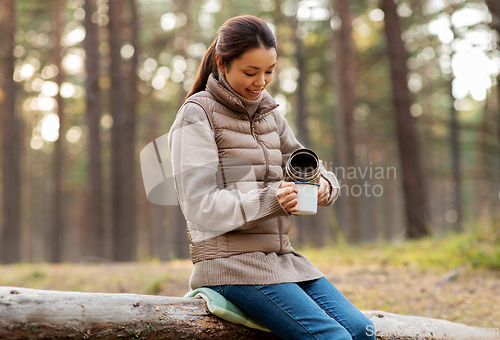 Image of asian woman with thermos drinking tea in forest