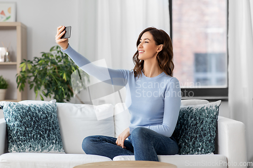 Image of happy woman with smartphone taking selfie at home