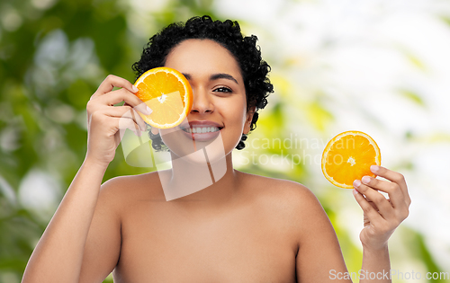 Image of smiling african woman making eye mask of oranges