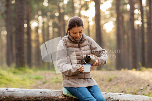 Image of asian woman with thermos drinking tea in forest