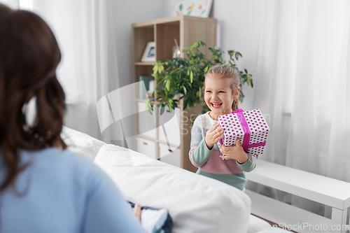 Image of happy daughter giving present to mother at home