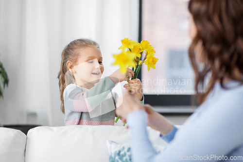 Image of happy daughter giving daffodil flowers to mother