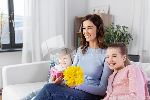 Image of daughters giving flowers and gift to happy mother