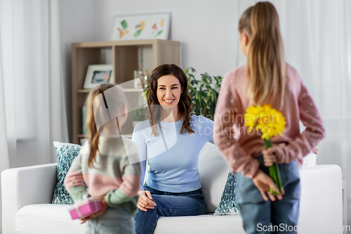 Image of daughters giving flowers and gift to happy mother