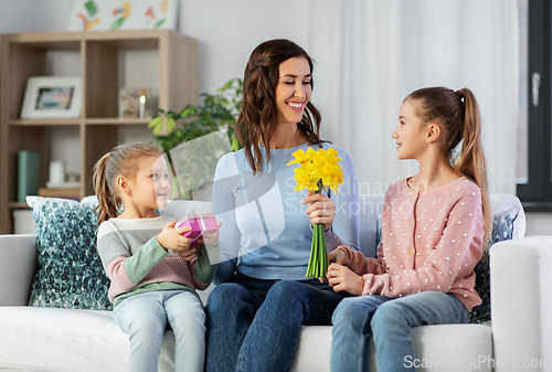 Image of daughters giving flowers and gift to happy mother