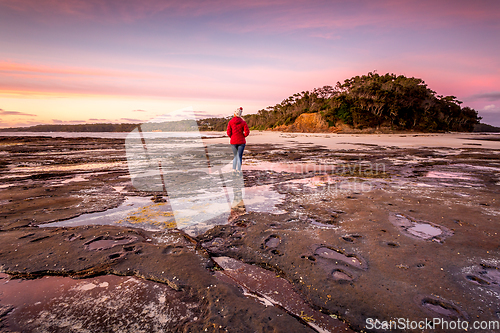 Image of Woman watching the sunrise from the outer rocky reef