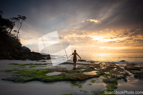 Image of A woman stands on the beach admiring the sunrise