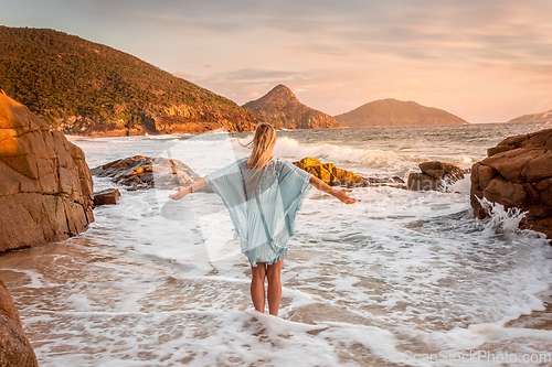 Image of Woman stands in ocean wabes with a soft pastel sunrise sky