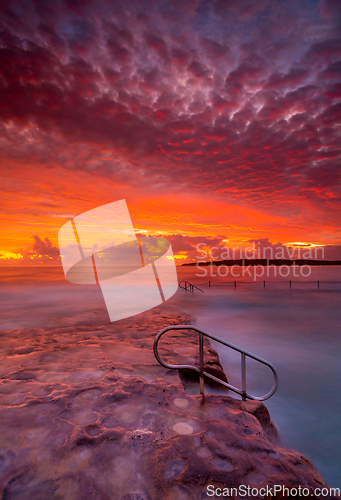 Image of Rich red stunning sunrise over rock pool and ocean