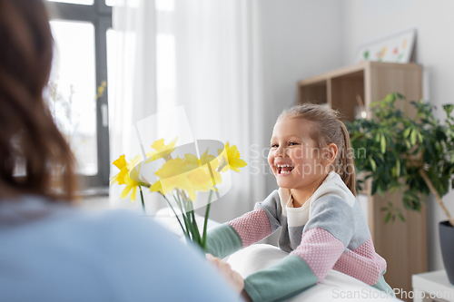 Image of happy daughter giving daffodil flowers to mother