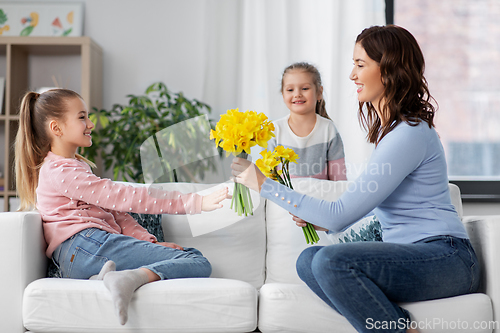 Image of daughters giving daffodil flowers to happy mother