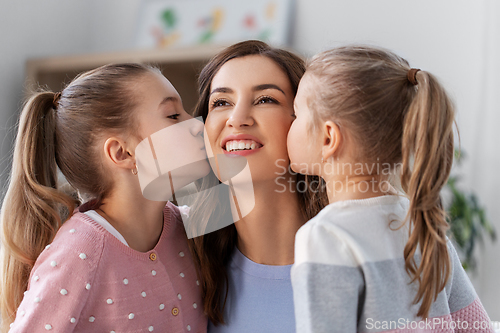 Image of happy mother and two daughters kissing her at home