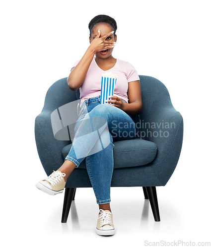 Image of scared woman eating popcorn sitting in armchair