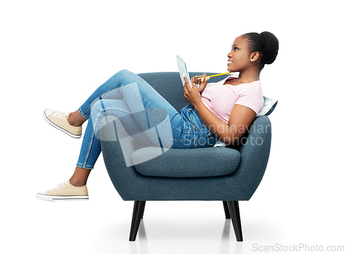 Image of happy young woman in armchair writing to notebook