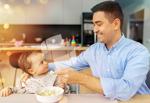 Image of happy father feeding baby in highchair at home