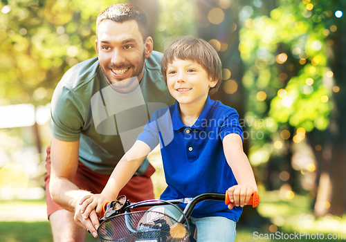 Image of father teaching little son to ride bicycle at park