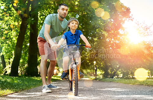 Image of father teaching little son to ride bicycle at park