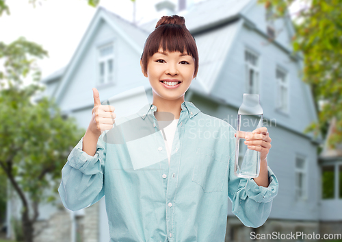 Image of happy asian woman holding glass bottle with water