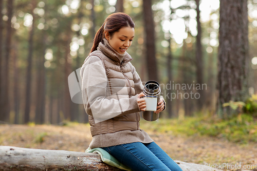 Image of asian woman with thermos drinking tea in forest