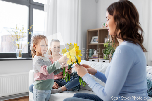 Image of daughters giving daffodil flowers to happy mother