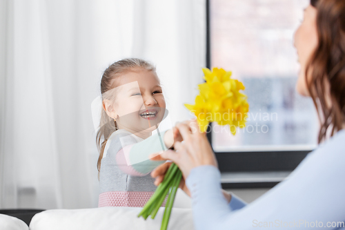 Image of happy daughter giving daffodil flowers to mother