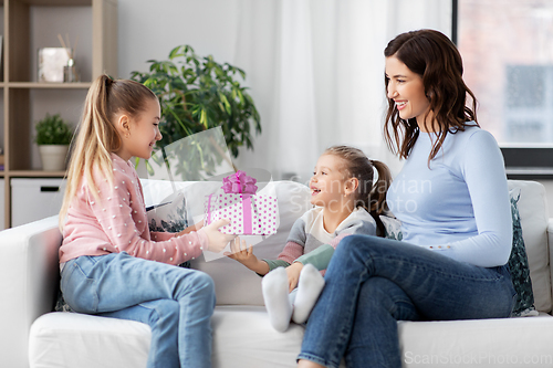 Image of girl giving present to younger sister at home