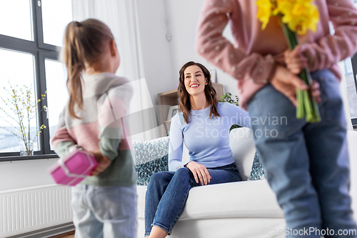 Image of daughters giving flowers and gift to happy mother