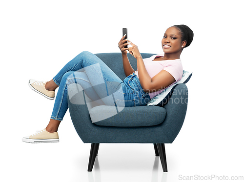 Image of african american woman with smartphone in armchair