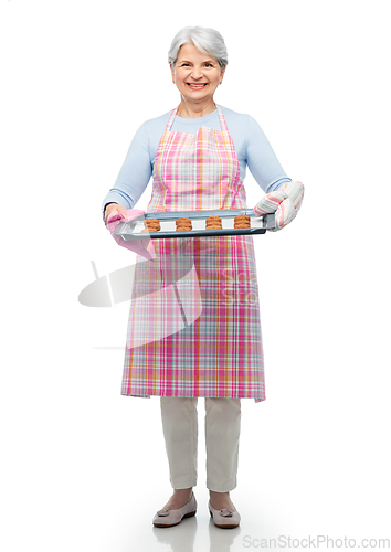 Image of senior woman in apron with cookies on baking pan