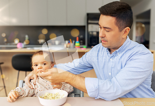 Image of middle-aged father feeding baby daughter at home