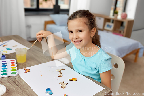 Image of little girl painting wooden items at home