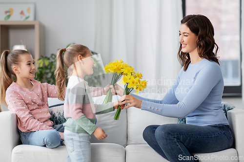 Image of daughters giving daffodil flowers to happy mother