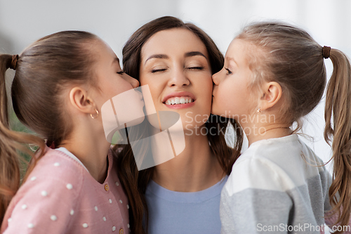 Image of happy mother and two daughters kissing her at home