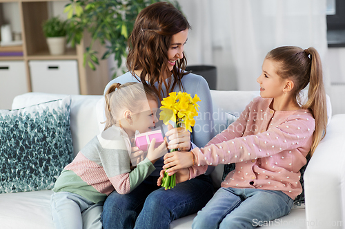 Image of daughters giving flowers and gift to happy mother