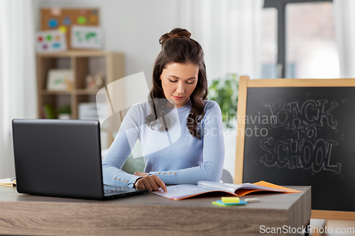 Image of teacher with laptop and notebook working from home