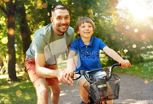 Image of father teaching little son to ride bicycle at park