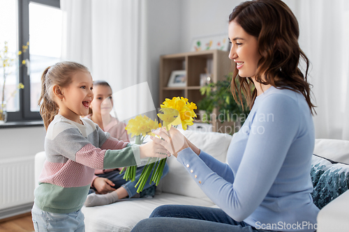 Image of daughters giving daffodil flowers to happy mother