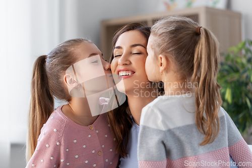 Image of happy mother and two daughters kissing her at home