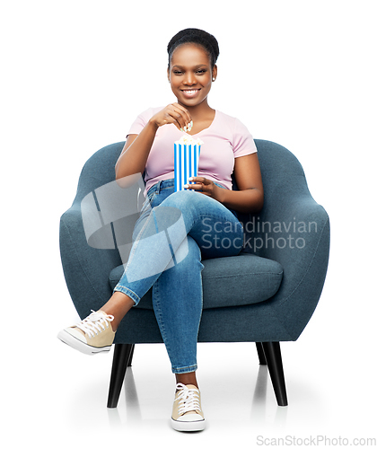 Image of african woman eating popcorn sitting in armchair