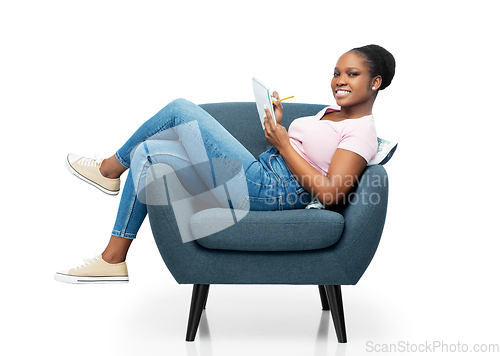 Image of happy young woman in armchair writing to notebook