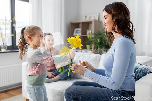 Image of daughters giving daffodil flowers to happy mother