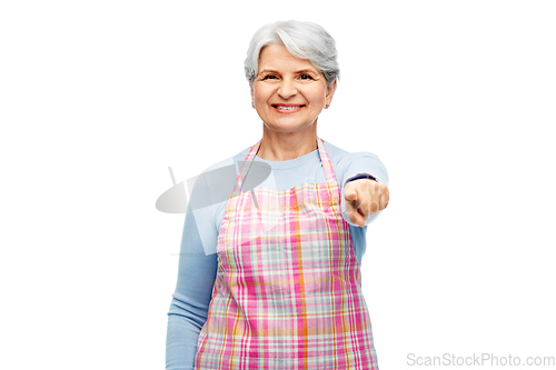 Image of smiling senior woman in apron pointing to camera