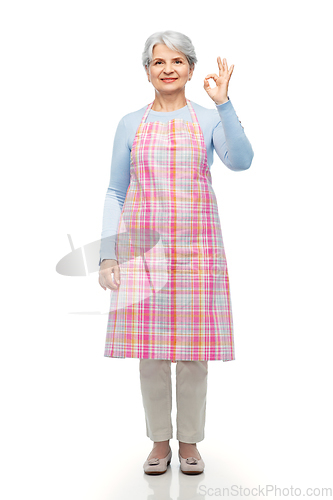 Image of smiling senior woman in apron showing ok gesture