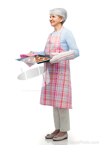 Image of senior woman in apron with cookies on baking pan