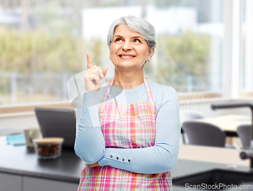Image of smiling senior woman in apron pointing finger up
