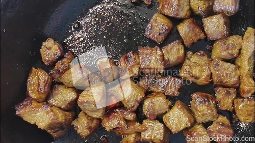 Image of Pieces of meat are fried in sizzling oil in a hot skillet. Bachelor breakfast, easy to cook food. The cook mixes the meat with a wooden spatula. Macro, close-up view. Frying meat, stove top.
