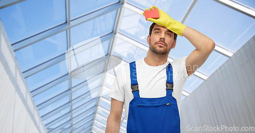 Image of tired male cleaner with sponge in glasshouse