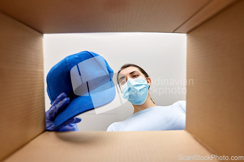 Image of woman in mask opening parcel box with clothes