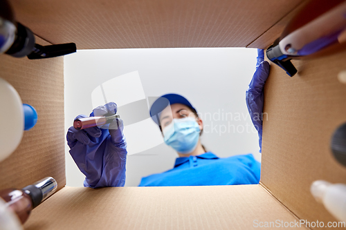 Image of woman in mask packing parcel box with cosmetics